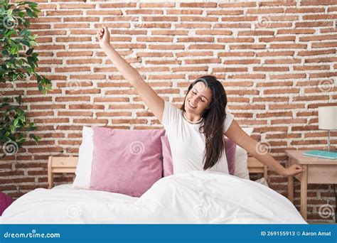 Young Beautiful Hispanic Woman Waking Up Stretching Arms At Bedroom