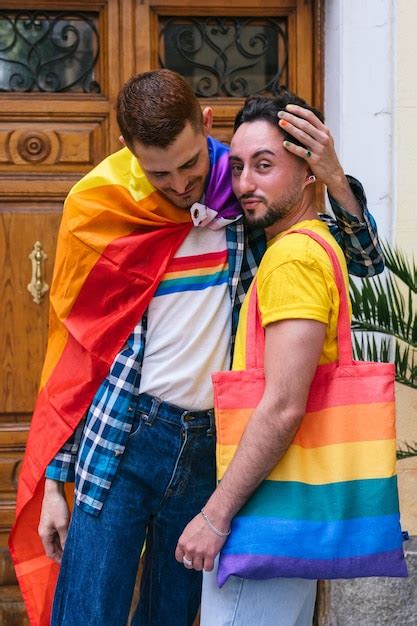 Abrazo orgulloso guapa pareja gay abrazándose en casa rodeada de símbolos lgbtq Foto Premium