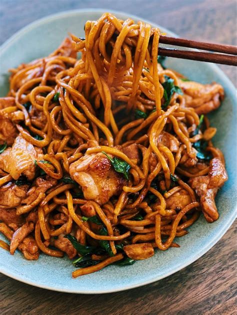 A Blue Plate Topped With Noodles And Meat Next To Chopsticks On A