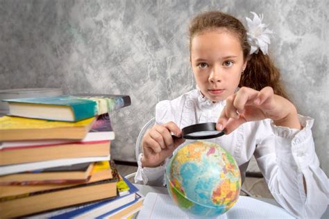 L écolière Dans L uniforme Scolaire Regardant Un Globe Par Une Loupe Et