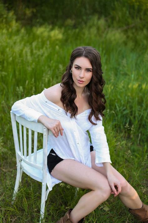 A Strict Beautiful Natural Brunette Girl In A Bright White Room Is Sitting On A Sofa In A Red