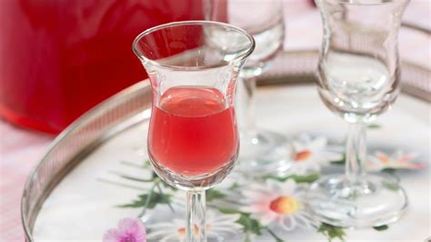 Two Wine Glasses On A Tray With Pink Liquid In Them And Flowers Around