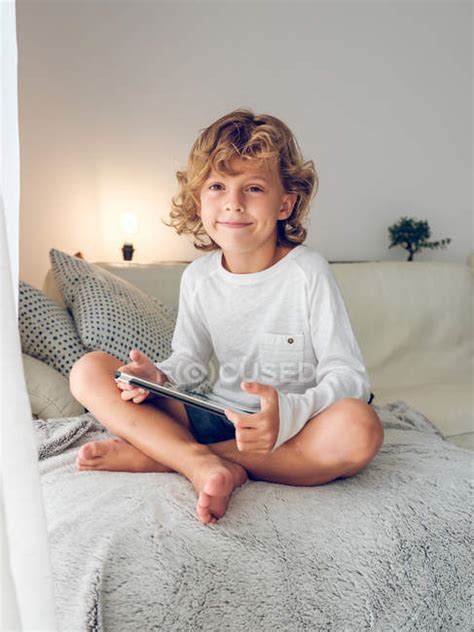 Cute Smiling Boy Sitting With Digital Tablet On Sofa Rest Couch