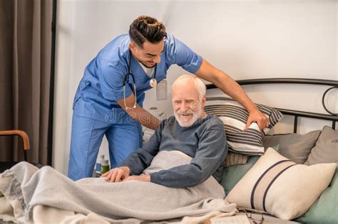 Healthcare Worker Helping A Bedridden Person Sit Up In Bed Stock Image