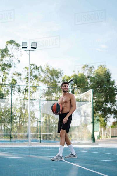 Concentrated Male Athlete With Naked Torso Playing Basketball Alone On Sports Ground In Summer