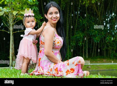 Portrait Of Latina Mother Sitting On Grass With Her Beautiful Brunette Baby Girl Standing