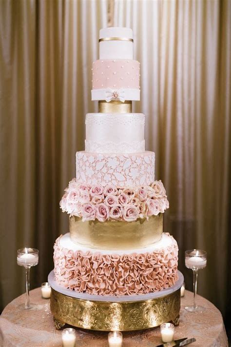 A Three Tiered Wedding Cake With Pink Flowers And Gold Trimmings On A Table