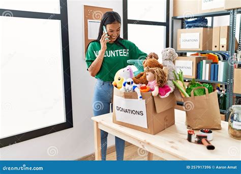 Joven Latina Con Uniforme De Voluntaria Hablando En El Smartphone Del Centro De Caridad Foto De