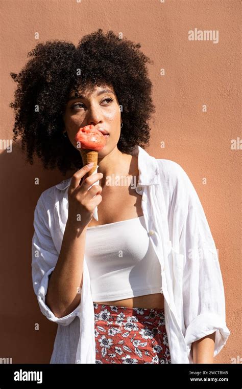 Curly Haired Black Woman In White Enjoys A Strawberry Ice Cream Cone