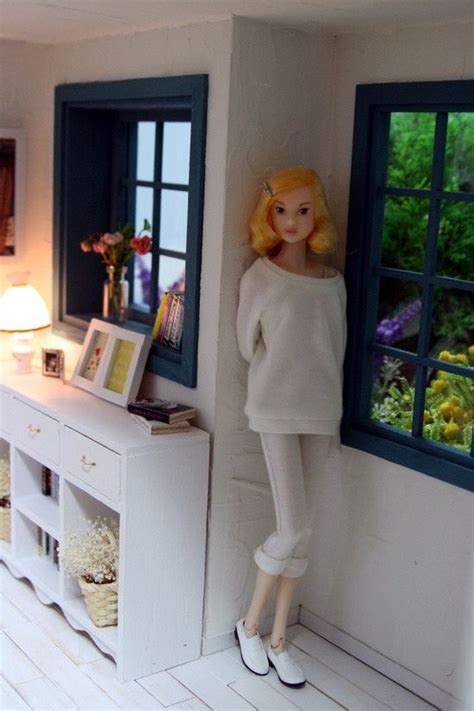 A Doll Is Standing Next To A Window In A Doll House With White