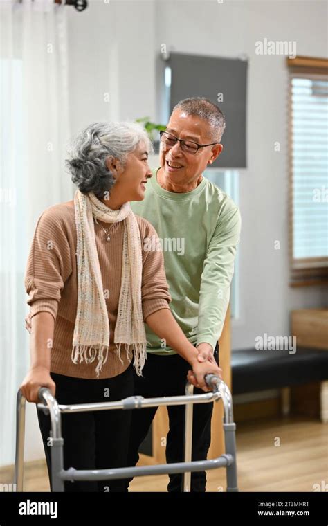 Caring Mature Man Helping His Wife Walking With Walker At Home Elderly