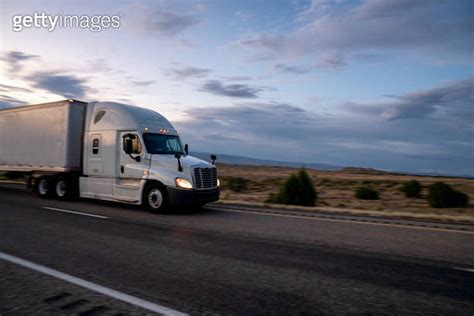 Semi Truck Speeding Down A Four Lane Highway With A Dramatic Sunset In