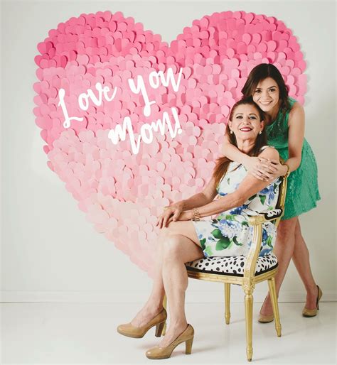 Two Women Sitting On A Chair In Front Of A Heart Made Out Of Paper Hearts