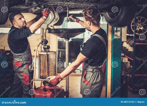 Car Mechanic Changing Motor Oil In Automobile Engine At Maintenance