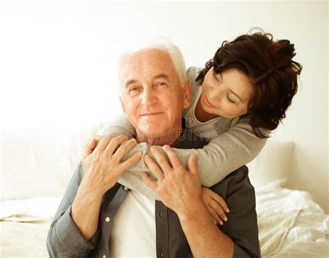 Mature 60 Year Old Couple Hugging While Sitting On The Bed In The Bedroom Stock Photo Image