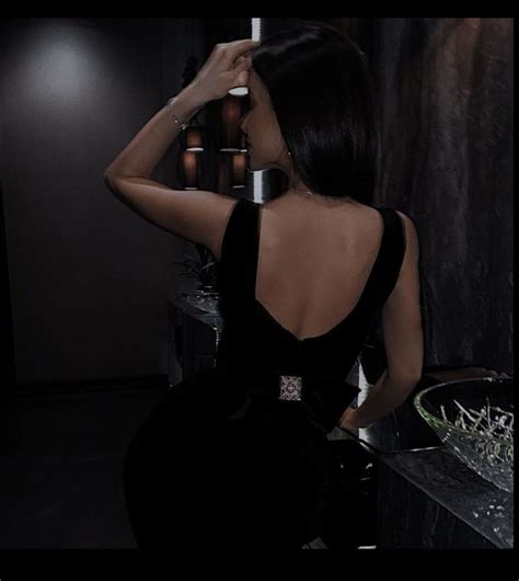 a woman in a black dress leaning against a wall with her back to the camera