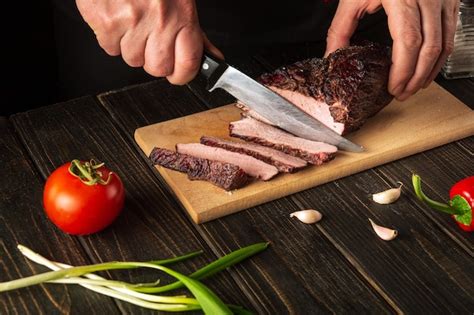 Premium Photo The Chef Cuts The Baked Beef Meat On A Cutting Board