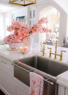 A White Kitchen With Pink Flowers On The Counter And Candles In Vases