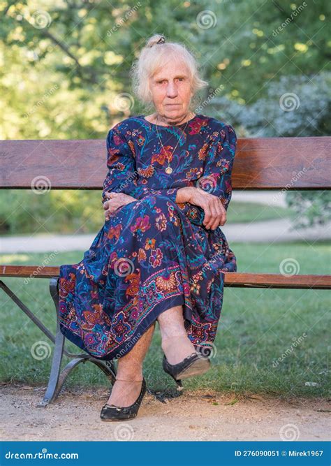 An Elegantly Dressed Elderly Woman Is Sitting On A Park Bench Stock