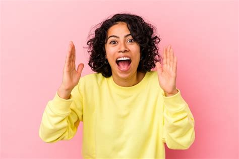 Jovem mulher latina encaracolada isolada no fundo rosa recebendo uma agradável surpresa