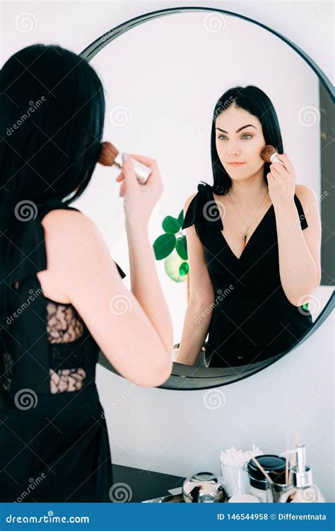 Beautiful Brunette With Long Hair Looking Into The Mirror And Doing Her Makeup Stock Photo