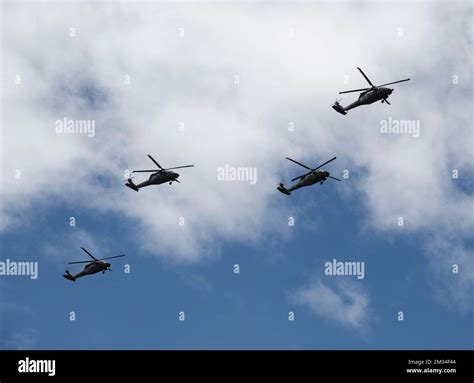 Four Black Hawk Helicopters Flying Over Crowd With Blue And Cloudy Sky