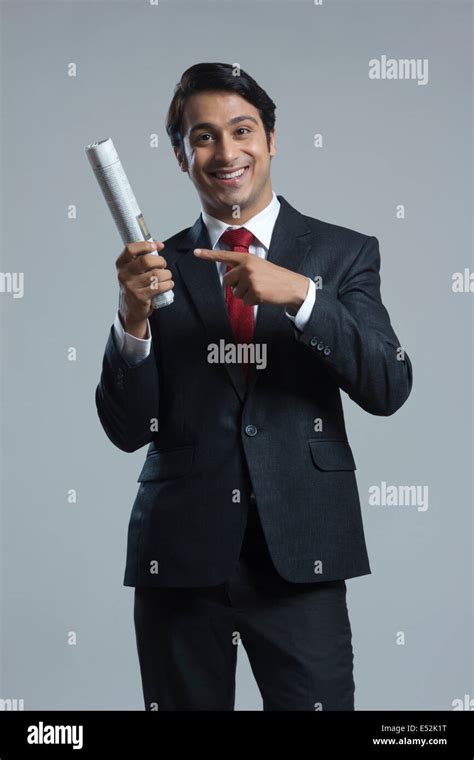 Portrait Of Happy Businessman Pointing At Newspaper Over Gray