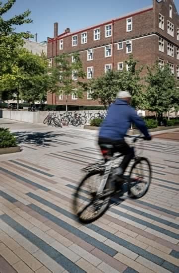 A Man Riding A Bike Down A Street Next To A Tall Brick Building With