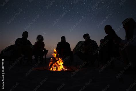 Group of friends gathering around bonfire in evening. Camping season ...