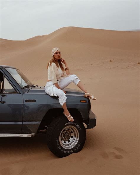 A Woman Sitting On The Hood Of A Truck In The Desert With Sand Dunes