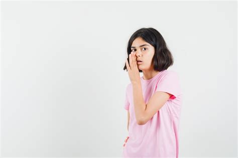 Menina contando o segredo por trás da mão em uma camiseta rosa vista