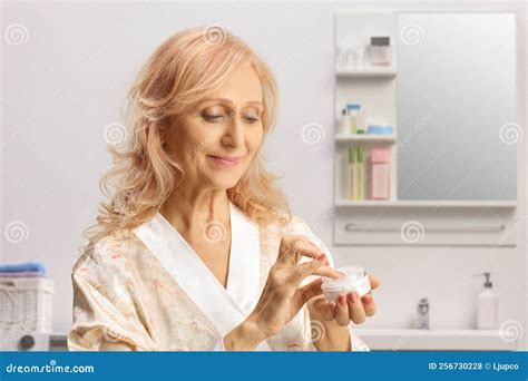 Mature Woman In A Bathrobe Holding A Face Cream In A Bathroom Stock