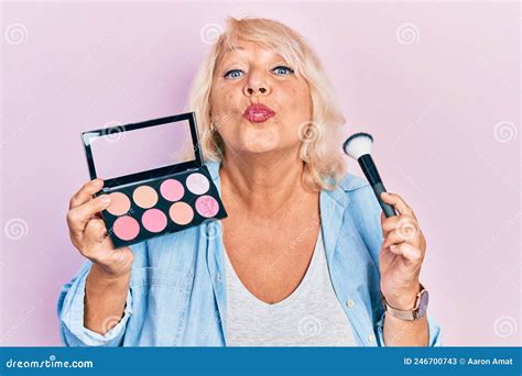Middle Age Blonde Woman Holding Makeup Brush And Blush Looking At The Camera Blowing A Kiss