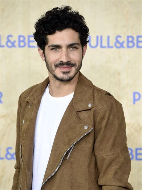 a man with curly hair wearing a brown jacket and white t - shirt is ...