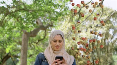 Animation Of Od Falling Emojis Over Woman In Hijab Using Smartphone