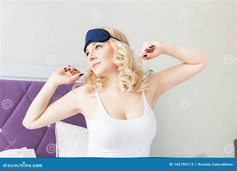 A Beautiful Blonde Woman Wakes Up And Snares A Mask For Sleeping In Her Bed In The Morning Stock