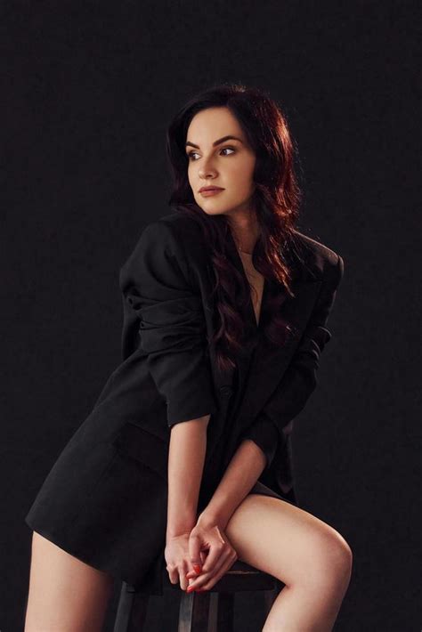 Sexy Brunette With Curly Hair In Luxury Clothes Sits On Chair In The Studio Against Black