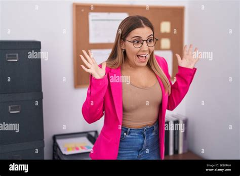 Junge blonde Frau im Büro steht feiert verrückt und erstaunt über den Erfolg mit erhobenen