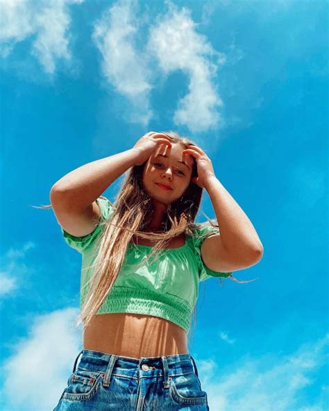 a young woman standing in front of a blue sky holding her hands to her head