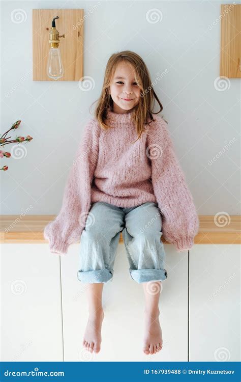 Smiling Little Barefoot Girl in Oversized Sweater Sitting on a Shelf at ...