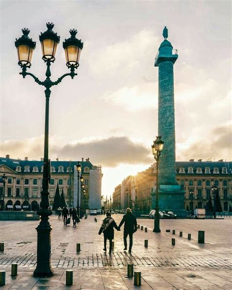 Two People Are Walking Down The Street In Front Of A Tall Light Pole