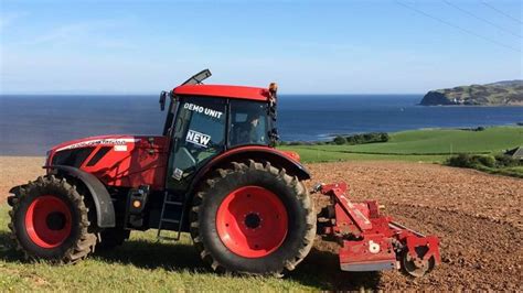 A Red Tractor Parked On Top Of A Field Next To The Ocean