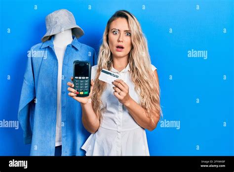 Schöne junge blonde Frau im Shop Assistance hält dataphone und Kreditkarte im Schockgesicht