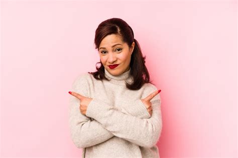 Mulher latina de meia idade isolada em pontos de rosa lateralmente está tentando escolher