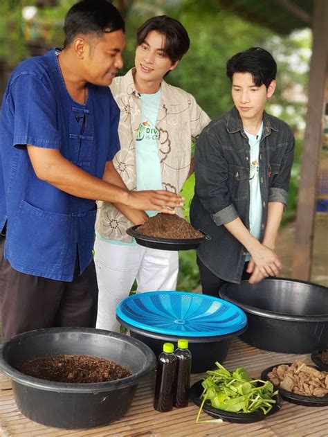 Two Men And A Boy Are Looking At Soil In Large Black Pans On A Wooden Table