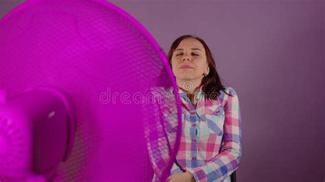 Acercamiento De Una Joven Sentada En Una Silla Frente A Un Ventilador Con Fondo Morado Brunette