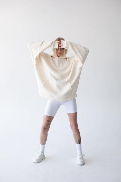 Une belle femme blonde posant dans un sweat à capuche blanc et des leggings posant sur un fond
