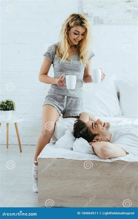 Blonde Woman Holding Cups With Coffee Near Happy Man Lying In Bed Stock