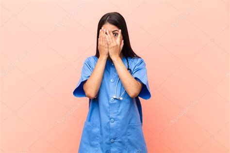 Joven Enfermera Latina Cubriendo La Cara Con Las Manos Asom Ndose Entre Los Dedos Con Expresi N