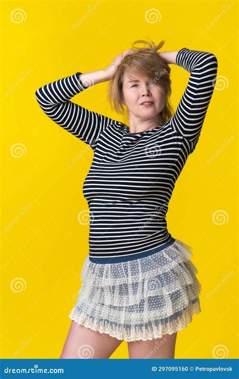 Mature Woman With Blond Hair Posing In Striped Long Sleeve And Mini Skirt Raising Hands Behind